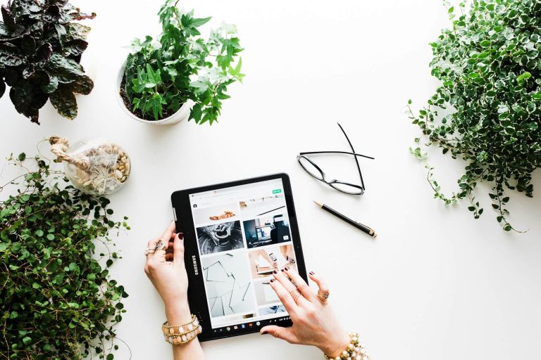 A person online shopping in their tablet with a great background filled with plants.